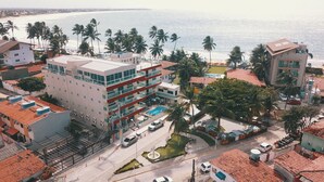 A multi-story hotel with a rooftop pool, surrounded by palm trees and a beach view. - Pousada Brasileira (Ipojuca)