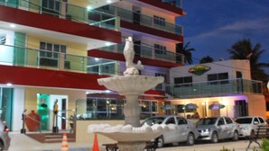 A multi-story hotel with a central fountain, outdoor seating, and a parking area. - Pousada Brasileira (Ipojuca)
