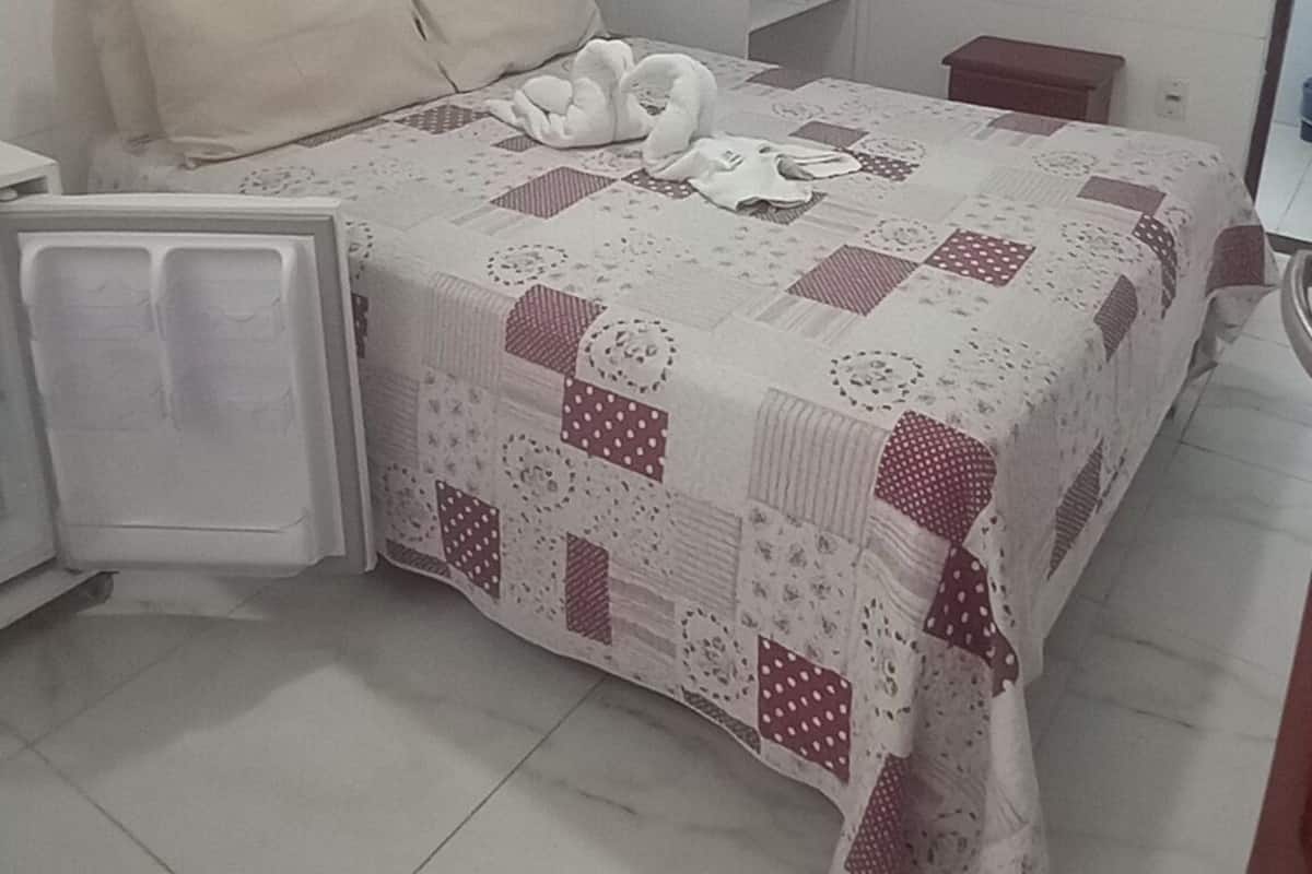 Une chambre à coucher comprenant un lit, une table de chevet, une commode, un radiateur et une fenêtre avec des rideaux.