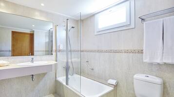 Un baño con ducha de vidrio, lavamanos blanco y retrete.