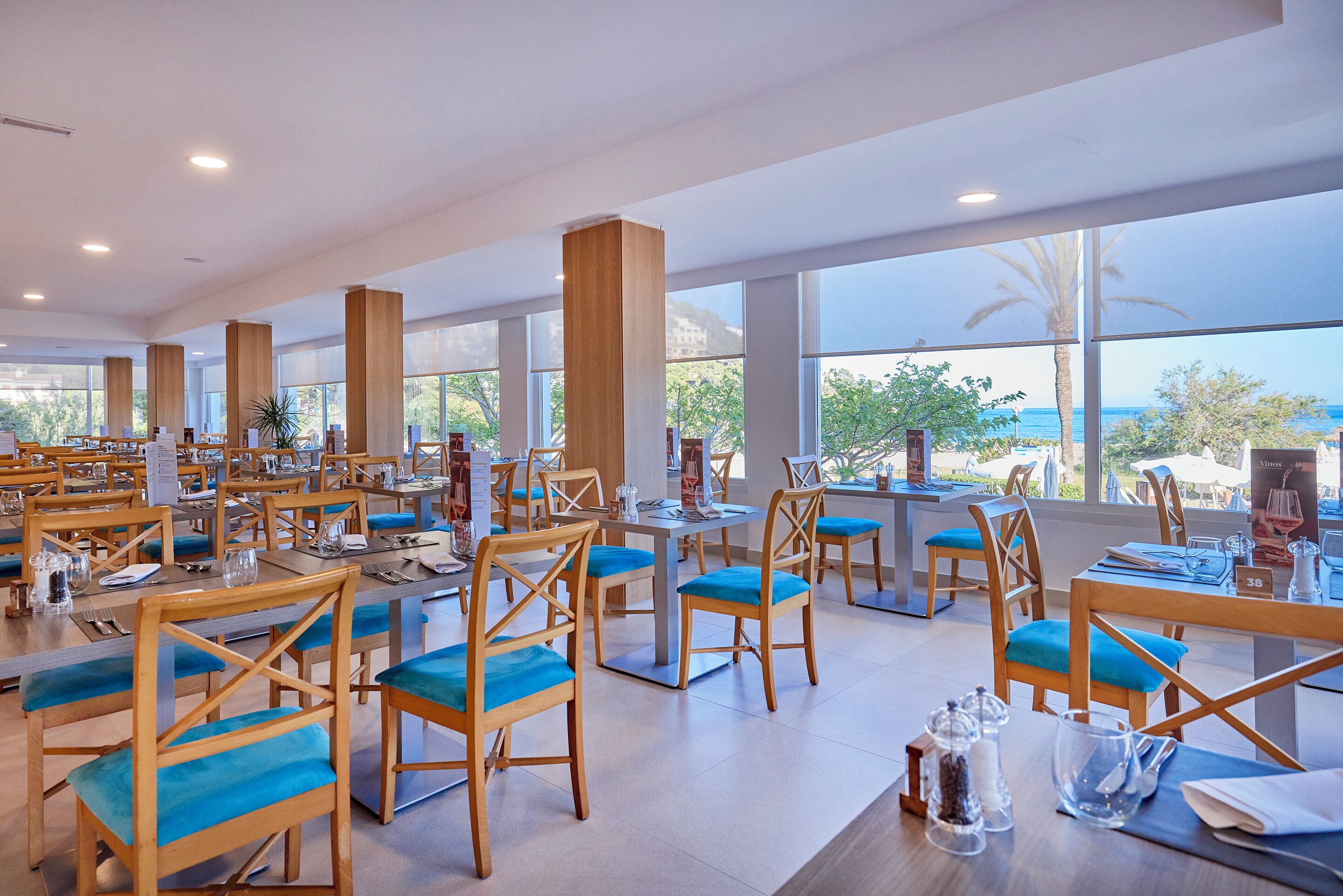 A spacious dining area with multiple tables and chairs, large windows with a view of the ocean, and a modern interior design.