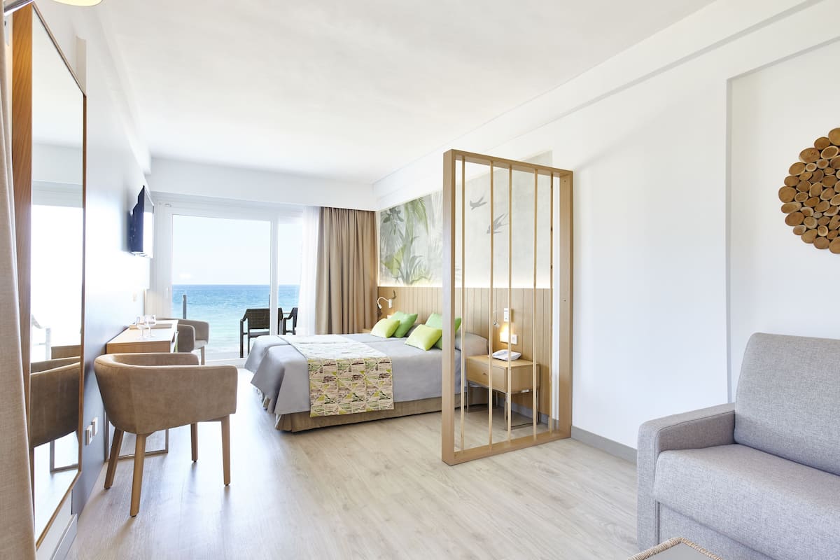 A modern hotel room with a bed, a desk, a chair, and a sofa.