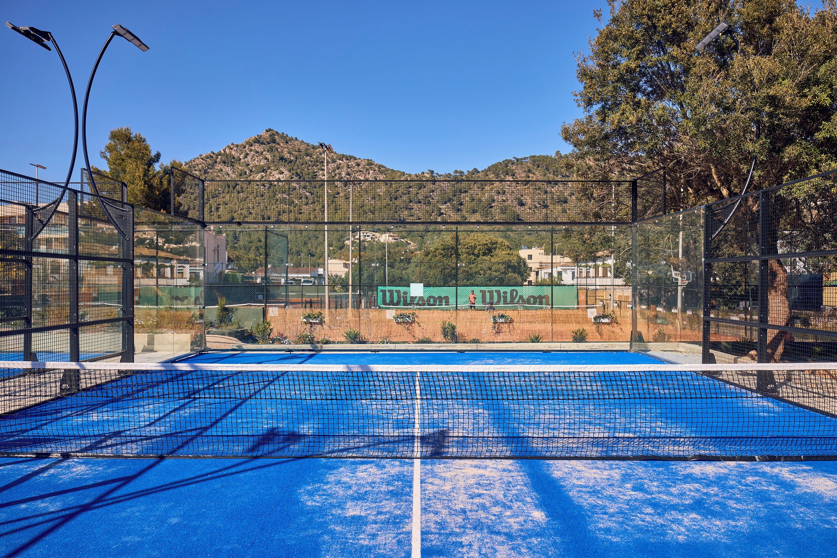 Una cancha de tenis con una red, rodeada por una valla, y una montaña al fondo.