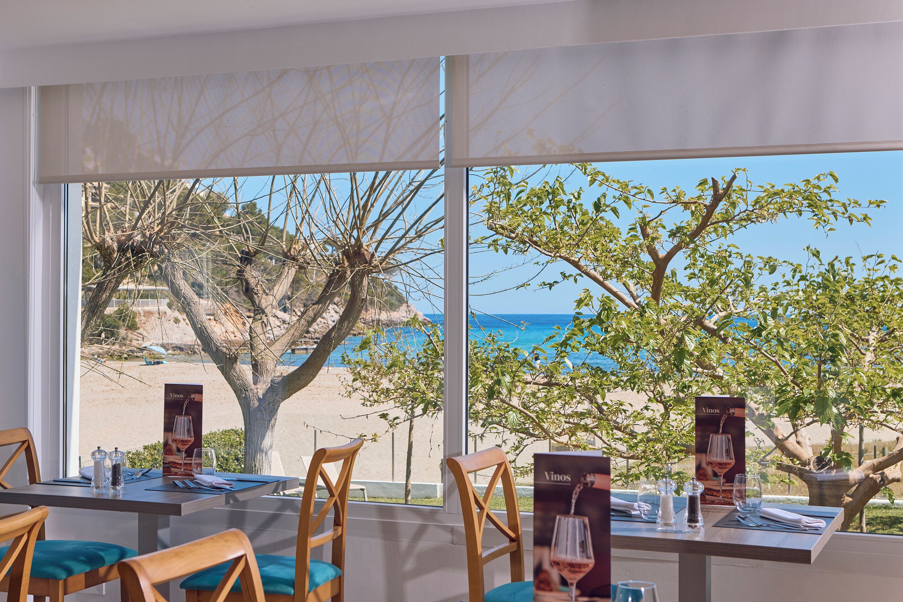 A dining area with tables set for two, a view of the beach, and a menu stand.