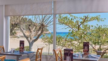 A dining area with tables set for two, a view of the beach, and a menu stand.