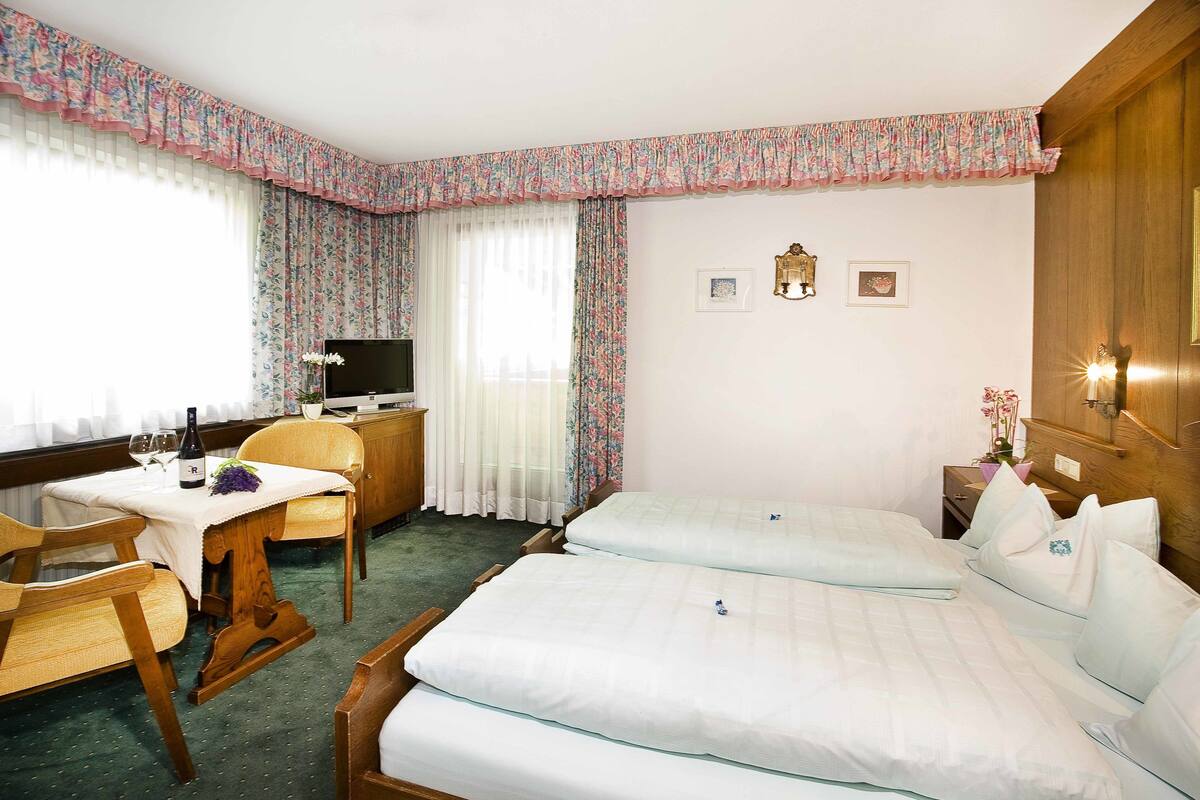 A hotel room with two beds, a wooden desk with a chair, a television, and a small table with a bottle and glasses.