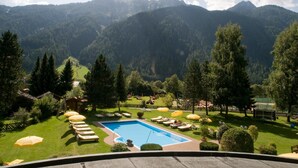 A pool area with lounge chairs and umbrellas, surrounded by a well-maintained lawn and trees, with mountains in the background. - Alpenhotel Fernau (Neustift Im Stubaital)