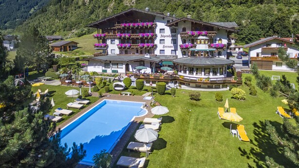 A large hotel with multiple balconies, a swimming pool, and a mountainous backdrop. - Alpenhotel Fernau (Neustift Im Stubaital)