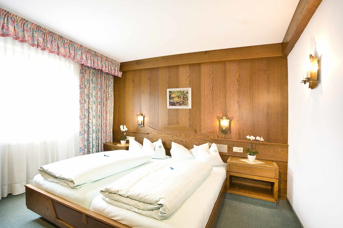 A double bed with a wooden headboard, two bedside tables with lamps, a floral curtain, and a framed picture on the wall.