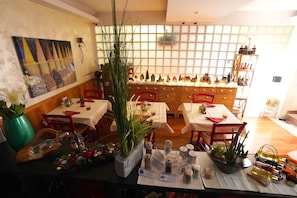 A restaurant with multiple tables, chairs, and a variety of decorative items including plants and bottles. - Bahnhof Haus (Chiasso)