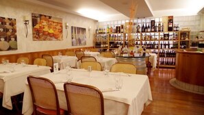 A restaurant with tables set for dining, a wine rack in the background, and a bar area. - Bahnhof Haus (Chiasso)