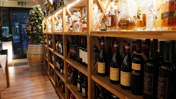 A wine cellar with wooden shelves stocked with various bottles. - Bahnhof Haus (Chiasso)