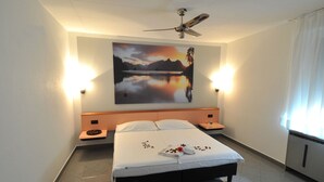A hotel room with a bed, nightstands, a ceiling fan, a painting of a landscape, and a window with curtains. - Bahnhof Haus (Chiasso)