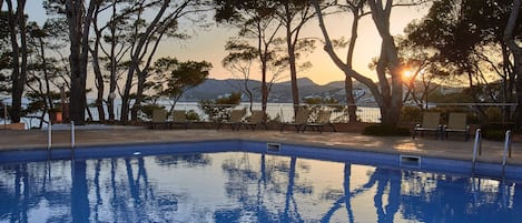 Piscina com água azul cristalina, rodeada por árvores e vista para montanhas ao fundo.