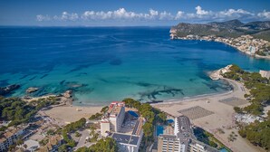 An aerial view of a coastal area with a beach, buildings, and a mountainous backdrop. - Universal Hotel Lido Park & Spa (Calvia)