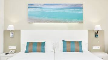 Habitación de hotel con una cama grande, dos lámparas de noche, un teléfono en la mesita y un cuadro de una playa en la pared.