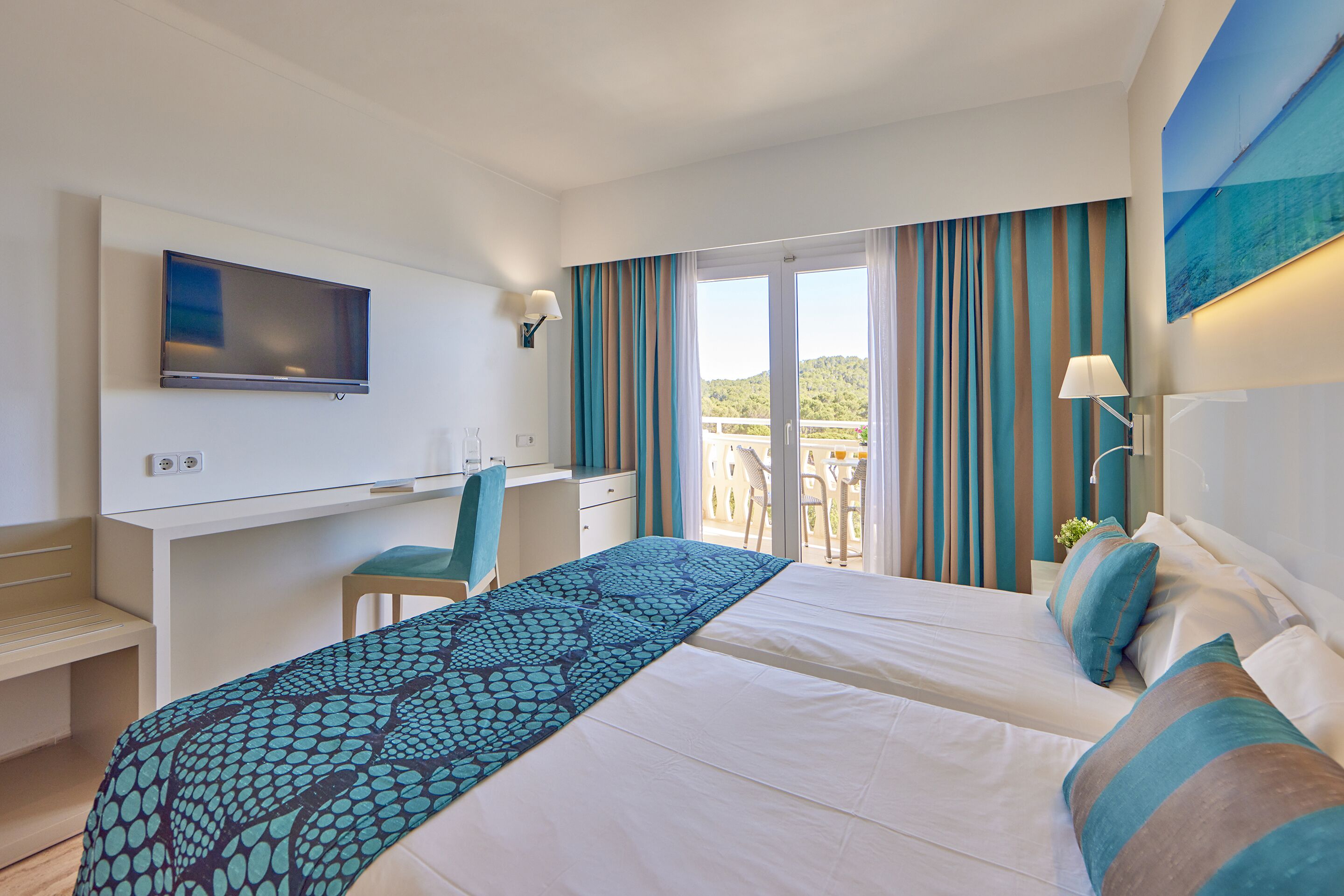 A hotel room with a bed, a desk, a television, and a balcony with curtains.