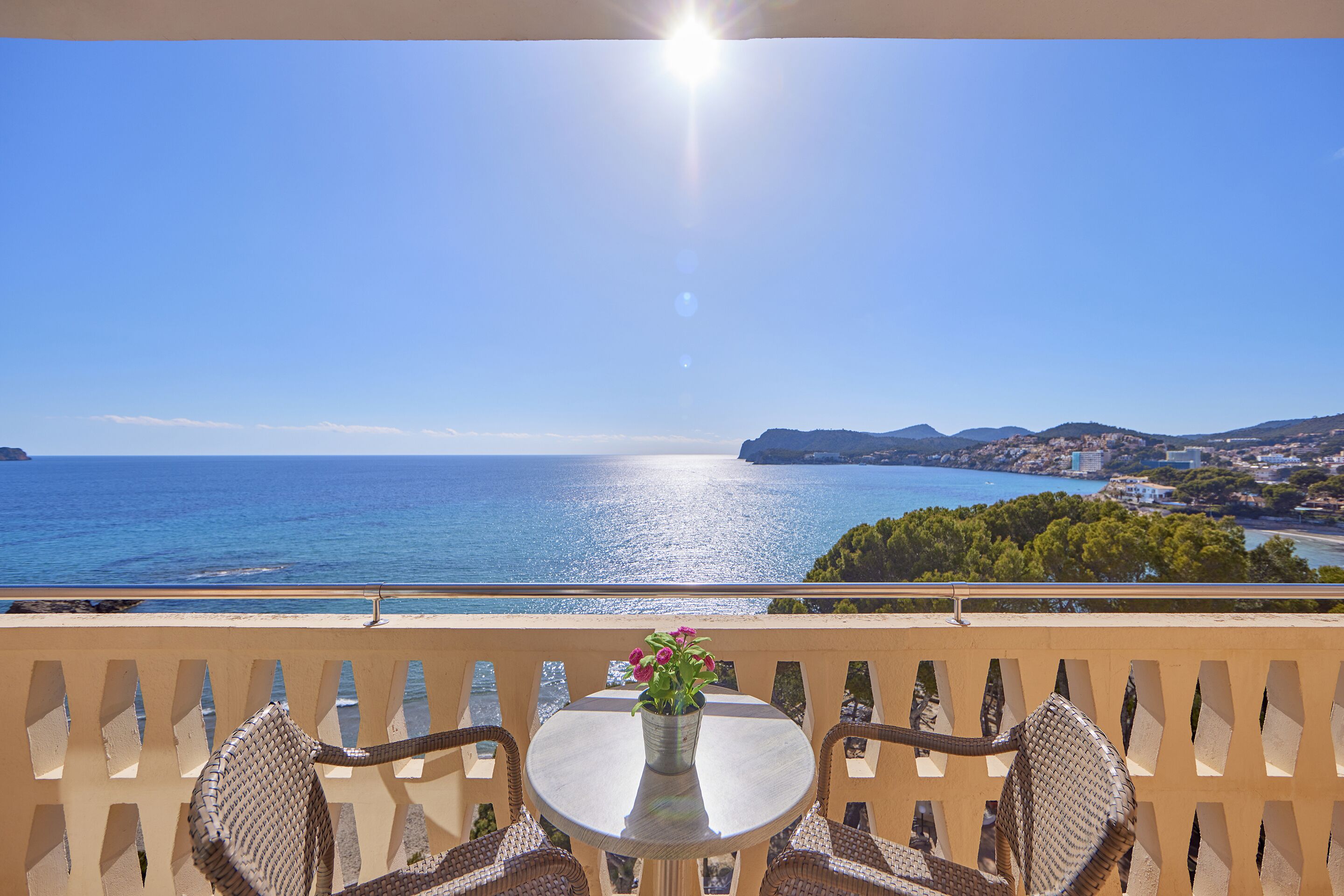 A balcony with a table and chairs overlooking a coastal view.