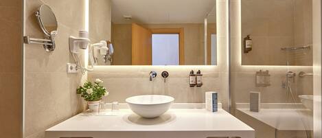 Un baño moderno con un lavabo blanco, un espejo, un cabezal de ducha de mano y una ducha con mampara de vidrio.
