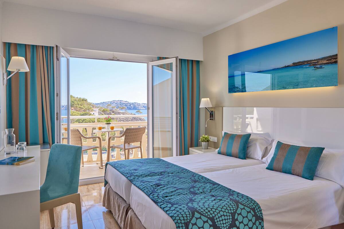 A hotel room with a large bed, a desk, and a balcony with a table and chairs.
