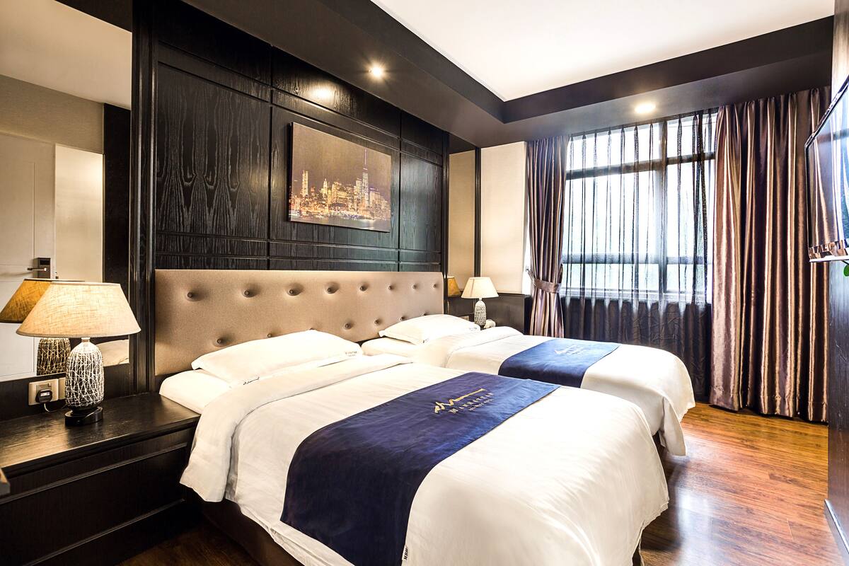 Une chambre d’hôtel avec deux lits, une grande œuvre d’art représentant un paysage urbain accrochée au mur et une vue sur la ville par la fenêtre.