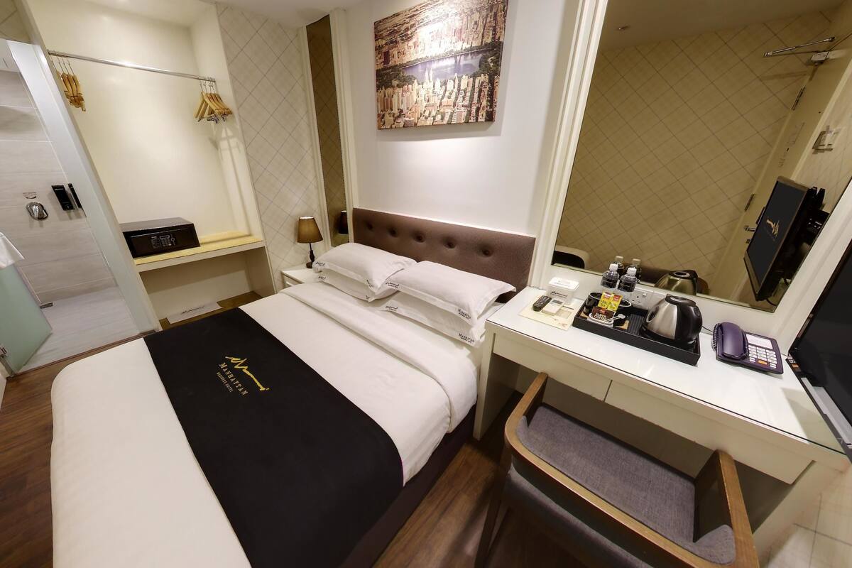 Une chambre d’hôtel comprenant un lit, un bureau, un miroir, un espace douche et une œuvre d’art représentant un paysage urbain accrochée au mur.