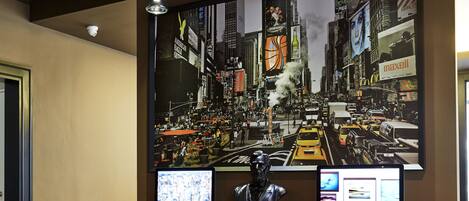 A reception area with a large cityscape artwork, two monitors, a sculpture, and red bar stools.