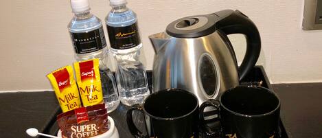 Un plateau contenant une cafetière, deux bouteilles d’eau, deux sachets de thé au lait, une tasse de café fort et deux tasses à café de marque.