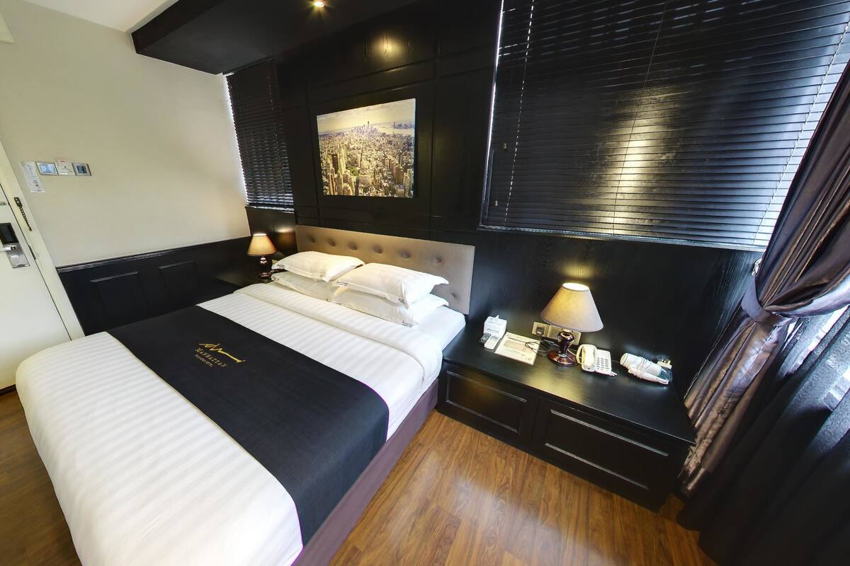 Une chambre d’hôtel avec un grand lit, une tête de lit ornée d’une image représentant un paysage urbain, une table de chevet avec une lampe et une porte avec une pancarte.