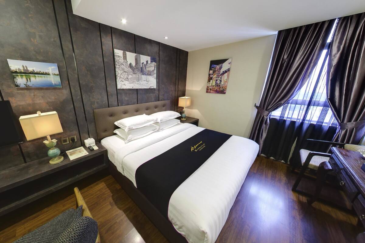 Une chambre d’hôtel avec un grand lit, un bureau, une chaise, une télévision et des œuvres d’art accrochées aux murs.