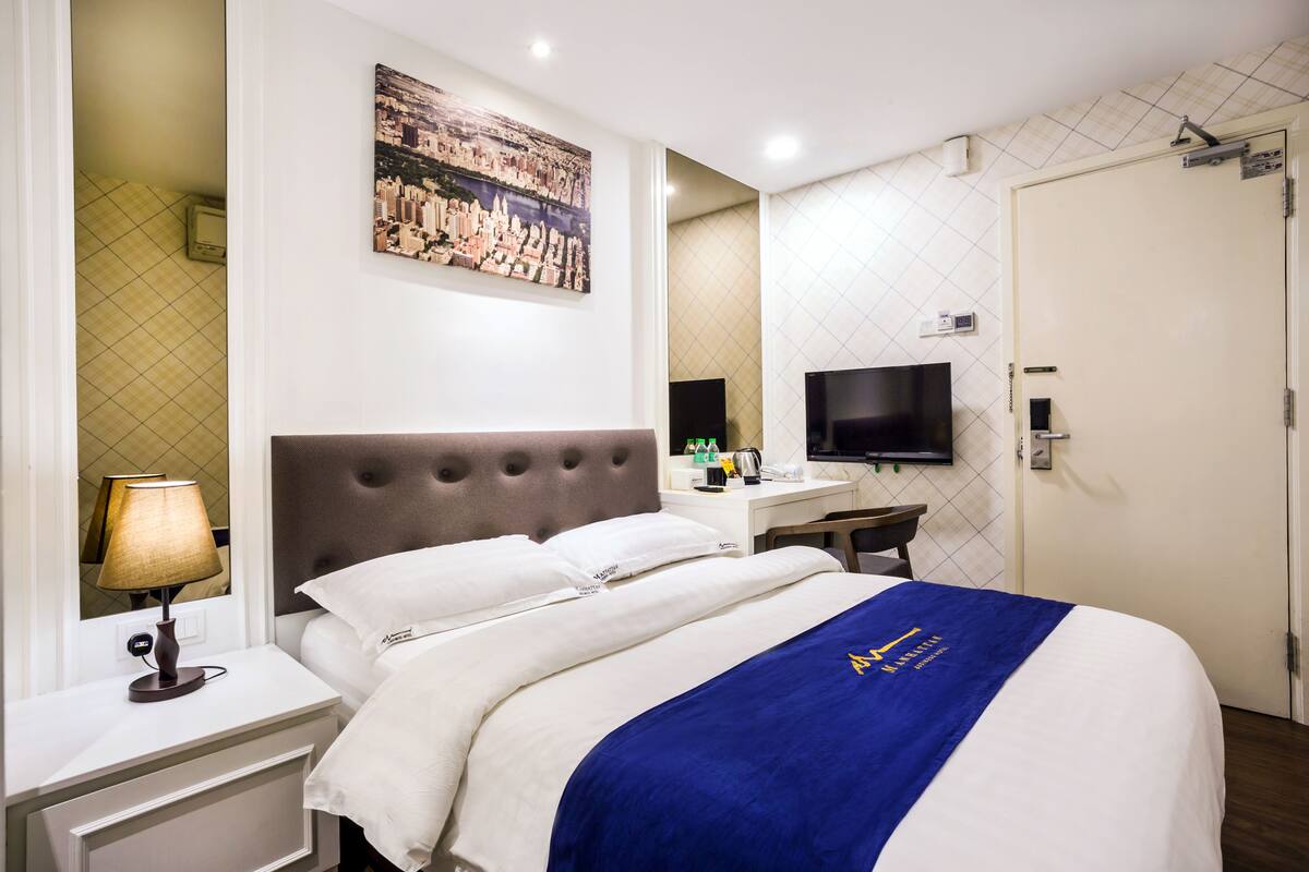Une chambre d’hôtel avec un lit, un bureau, une télévision et un tableau représentant un paysage urbain accroché au mur.