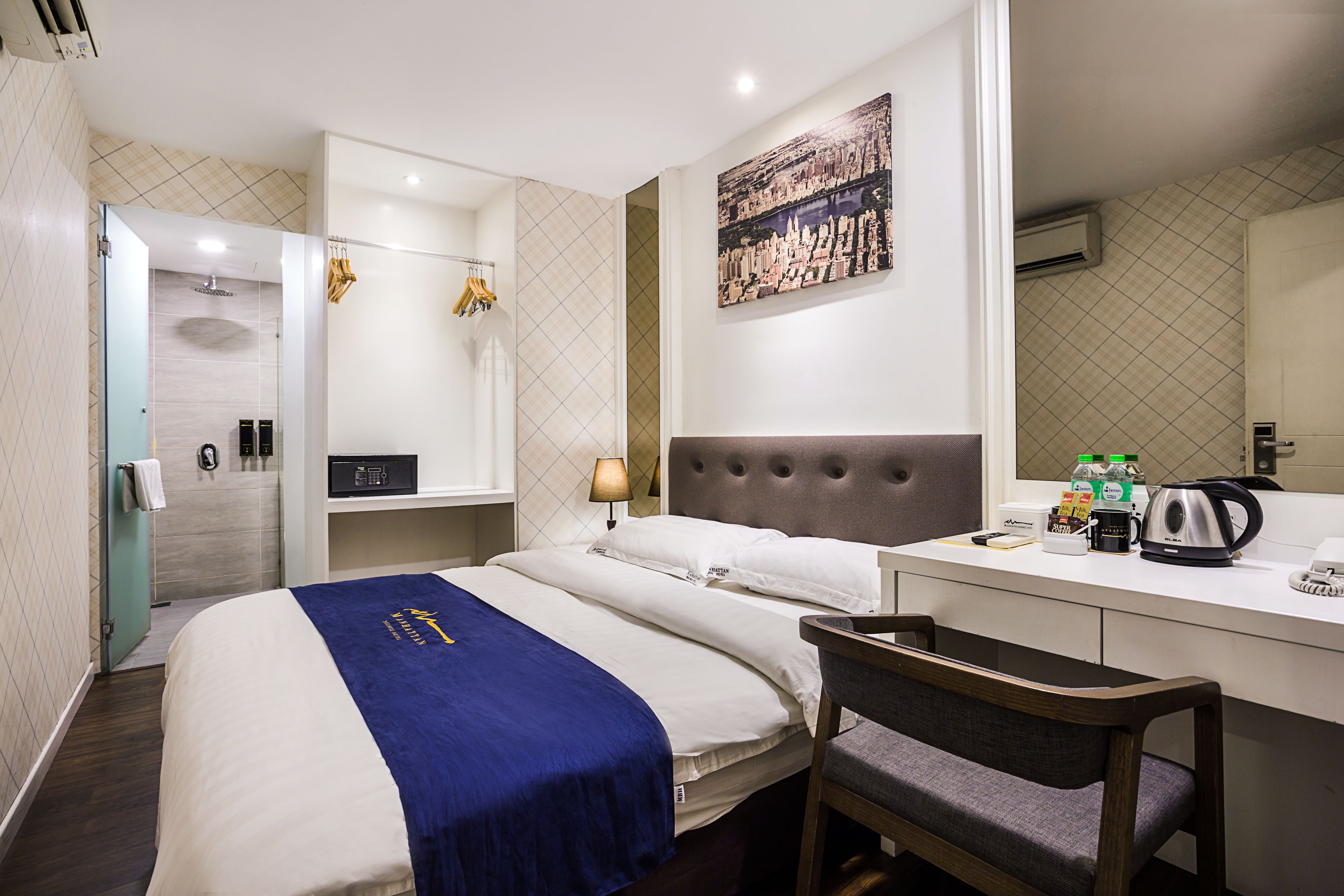 A hotel room with a bed, a desk with a chair, a coffee maker, and a painting on the wall.