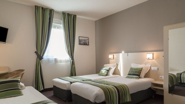 Une chambre d’hôtel avec deux lits, un téléviseur à écran plat, une fenêtre avec des rideaux, un tableau accroché au mur et des lampes de chevet.