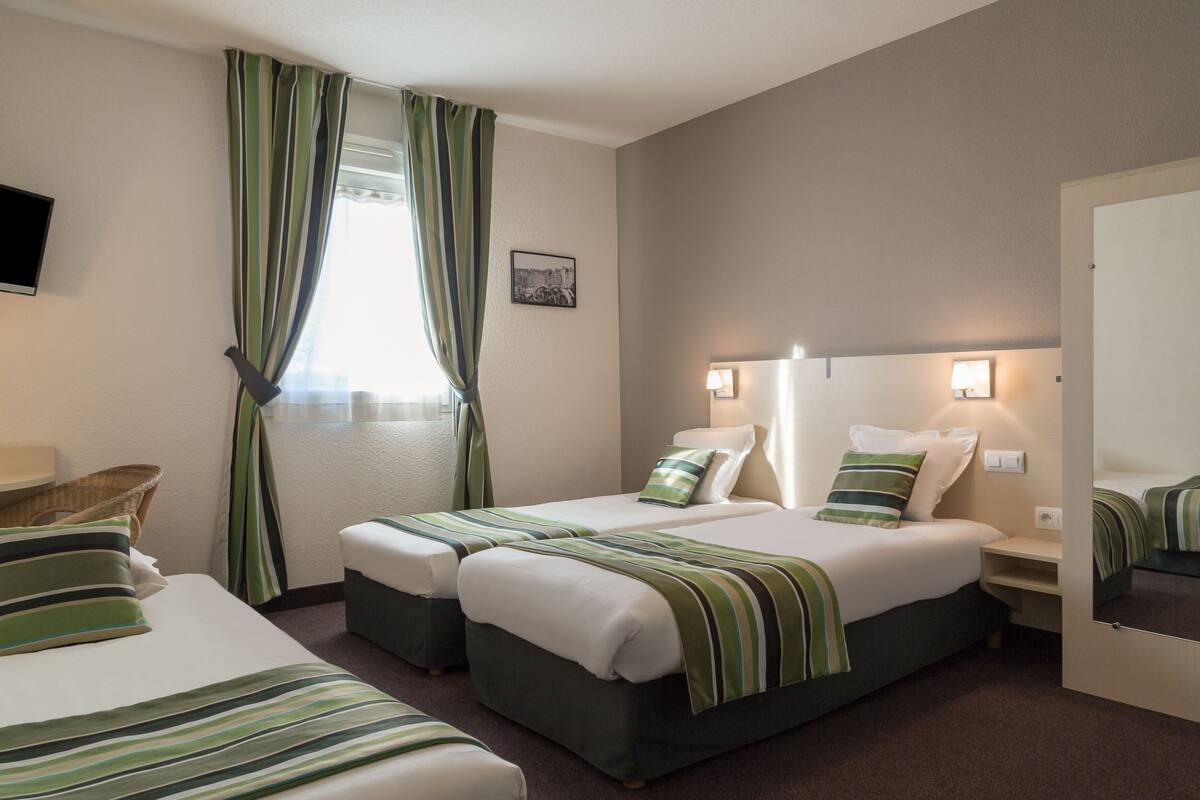 Une chambre d’hôtel avec deux lits, un téléviseur à écran plat, une fenêtre avec des rideaux, un tableau accroché au mur et des lampes de chevet.