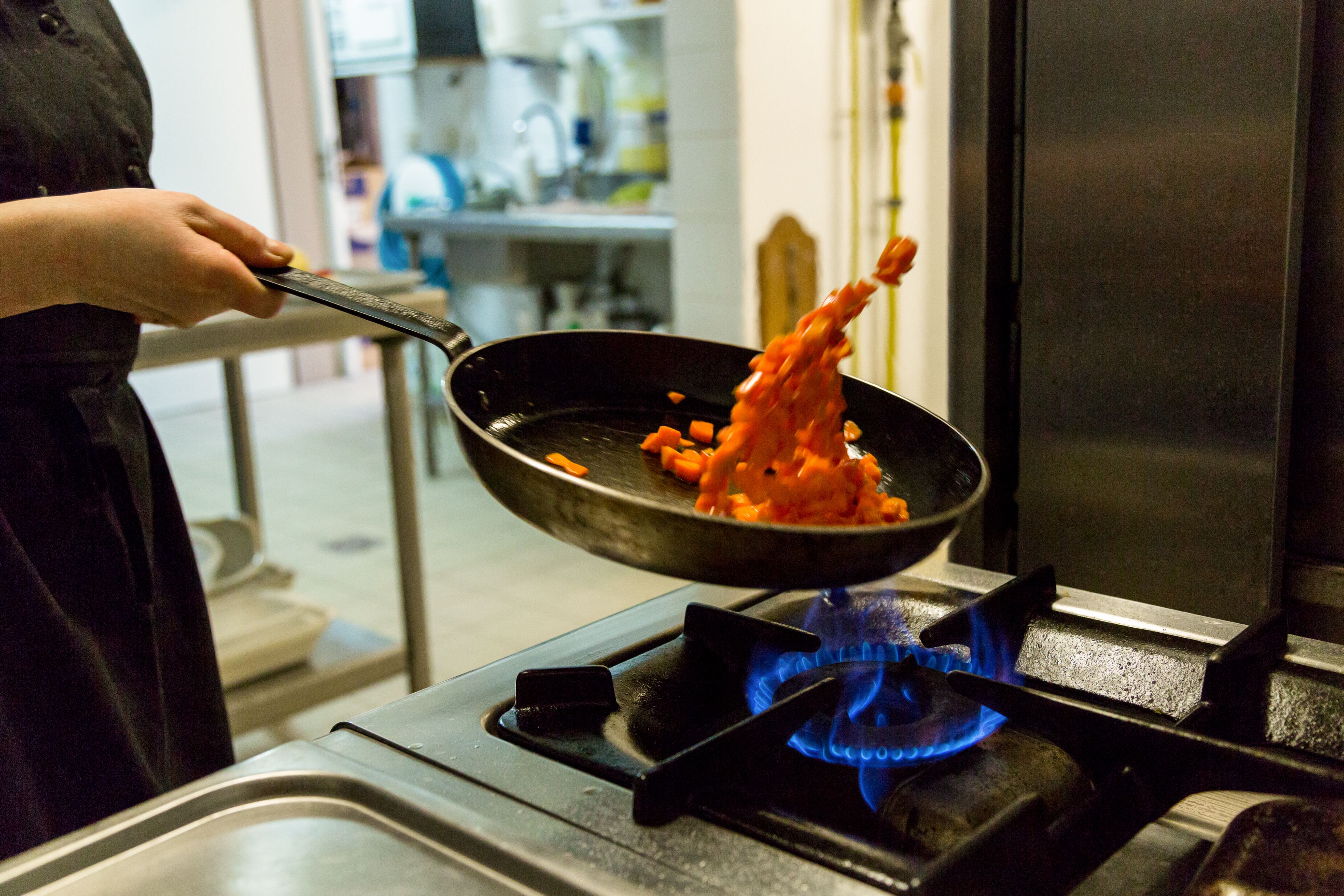 A person cooking with a pan on a gas stove.