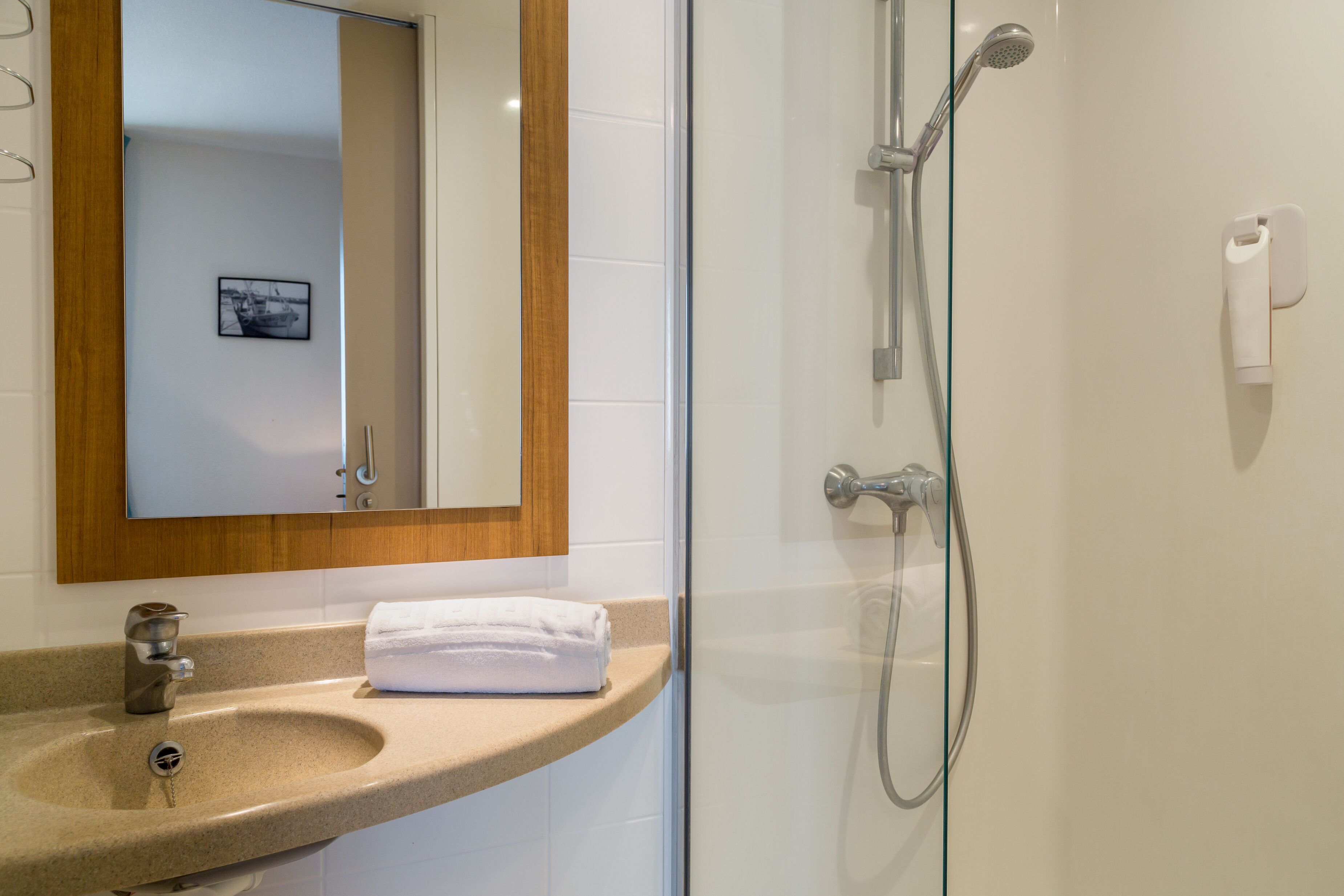 Un baño con cabina de ducha de vidrio, lavabo con toalla y espejo con marco de madera.