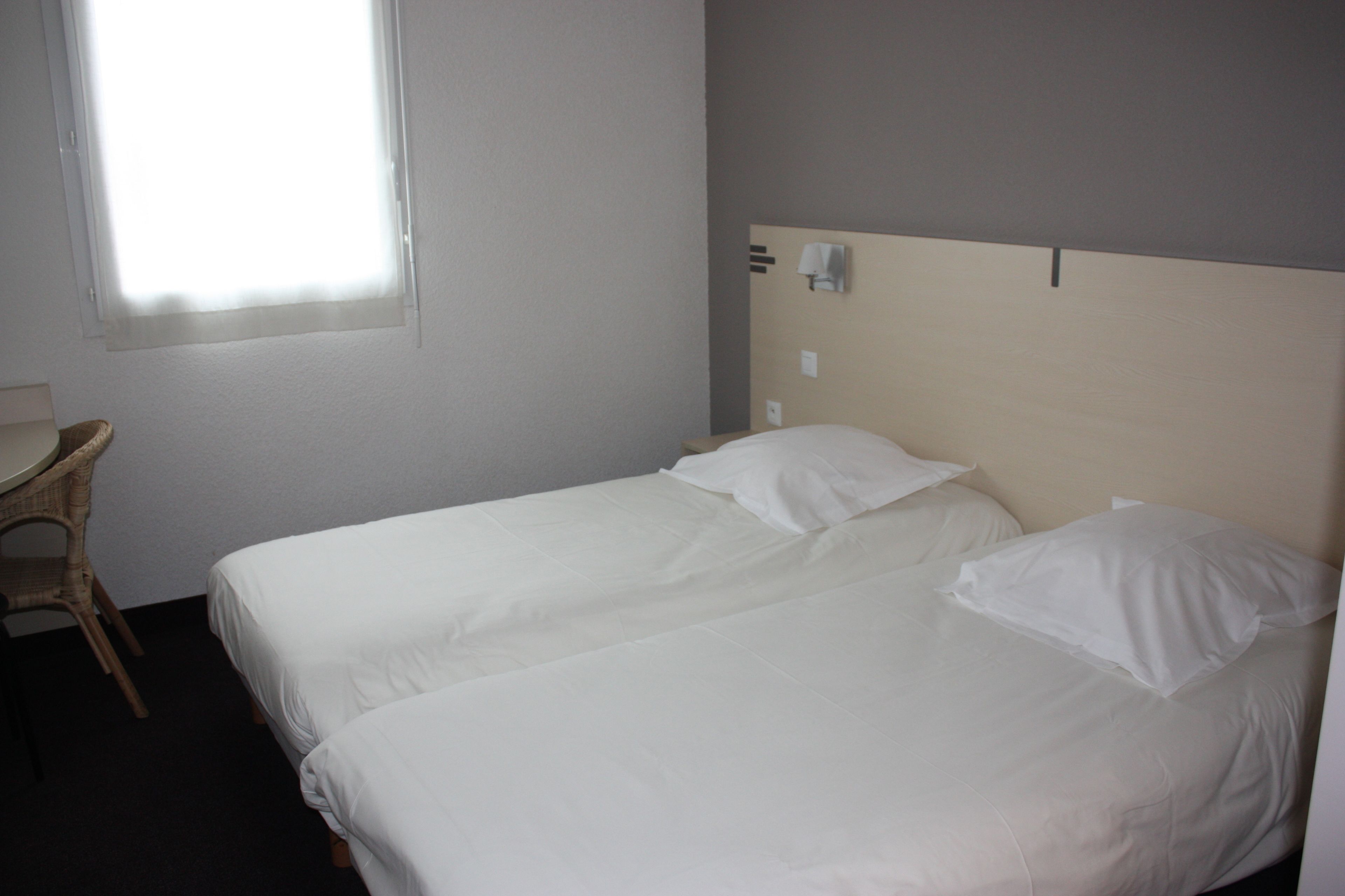 A hotel room with two single beds, a small table, and a window.