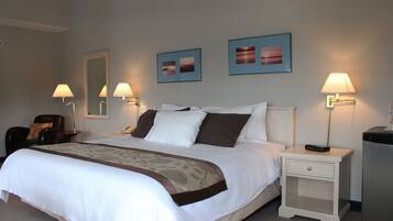 A neatly made bed with a white and brown bedspread, two bedside lamps, a nightstand with a drawer, and two framed pictures on the wall.