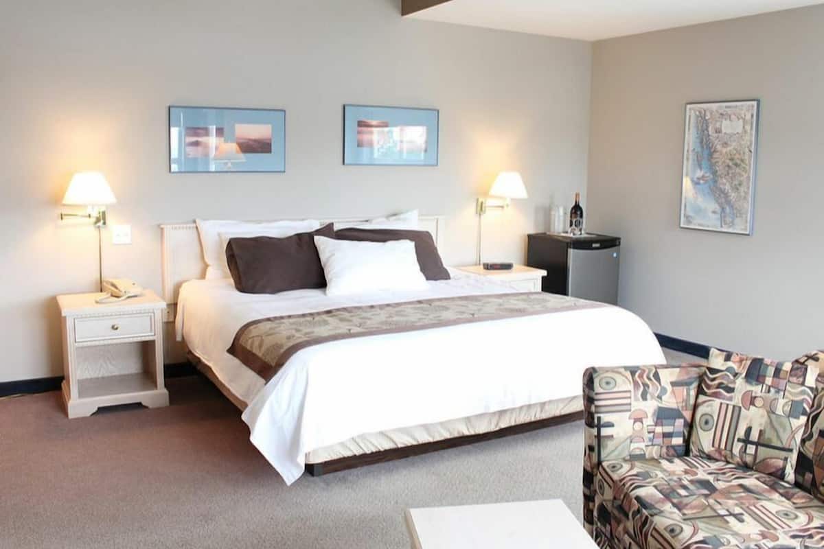 Quarto de hotel com uma cama, duas mesas de cabeceira, uma cadeira, um mapa na parede e uma luminária em cada mesa.