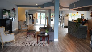 A spacious living area with a sofa, armchairs, and a coffee table. There is a reception desk with a plant and a stone wall. - Quarterdeck Inn Port Hardy (Port Hardy)