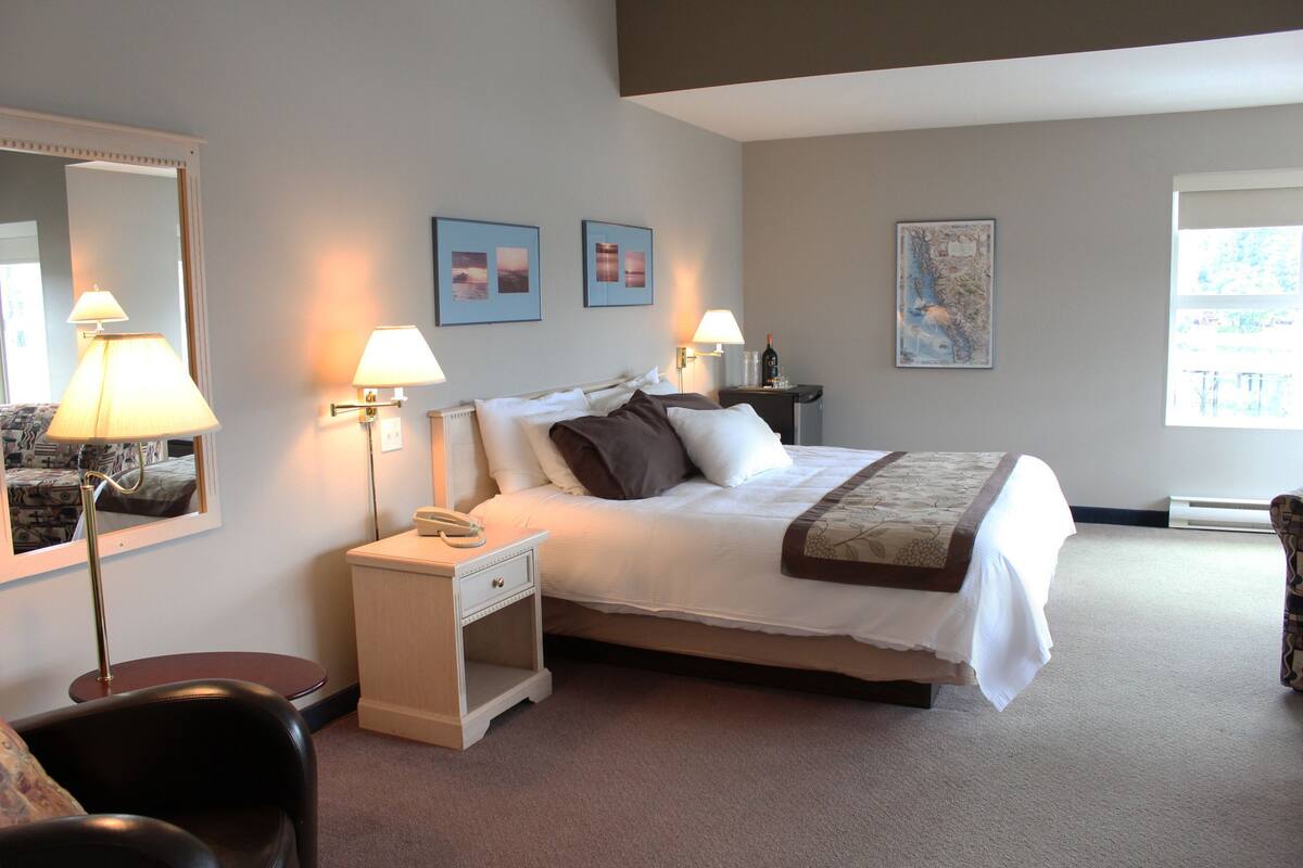 Quarto de hotel bem organizado, com cama, luminárias de cabeceira, mesa de cabeceira, cadeira e um espelho grande.