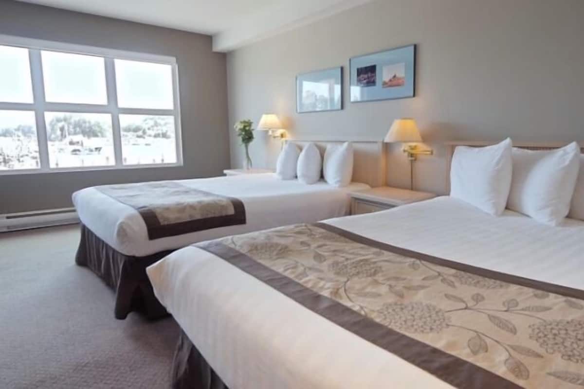 Quarto de hotel com duas camas, uma janela grande e vista para uma paisagem nevada.