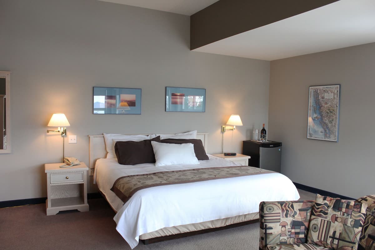 Quarto de hotel com uma cama, duas mesas de cabeceira, uma cadeira e obras de arte na parede.