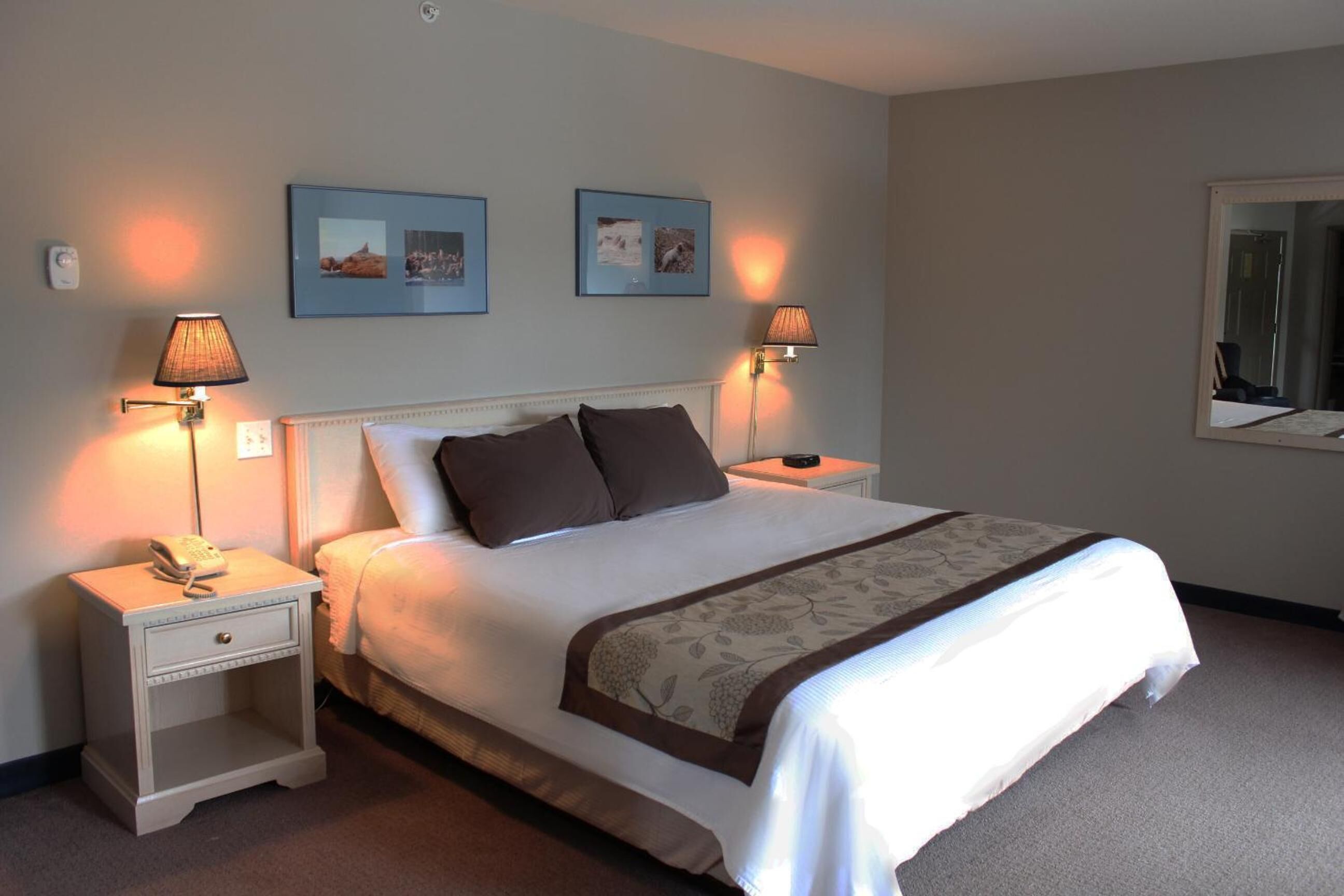 A neatly made bed with a white and brown bedspread, two bedside lamps, and two framed pictures on the wall.