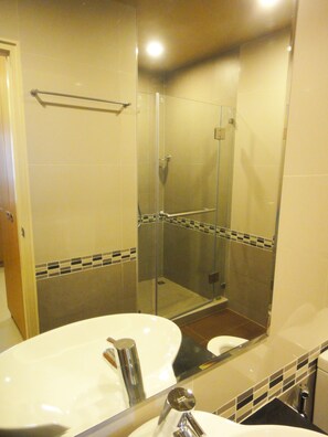 A bathroom with a glass-enclosed shower, a sink with a mirror, and tiled walls. - Aleaf Bangkok Hotel (Bangkok)