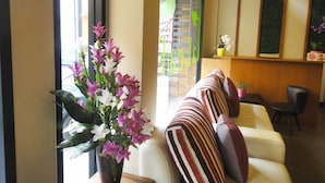 Un vestíbulo de hotel con un sofá, un jarrón de flores y una recepción.
