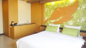 Un dormitorio con cama, un armario de madera, una pequeña kitchenette y una pared con diseño de hojas.