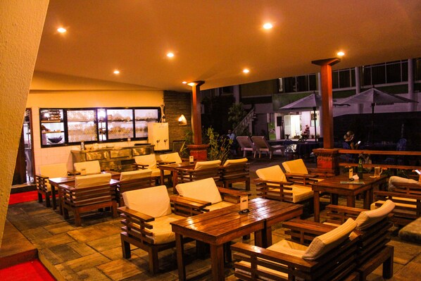 Ein Patio im Freien mit Holzmöbeln, darunter Tische und Stühle, und Blick ins hoteleigene Restaurant.
