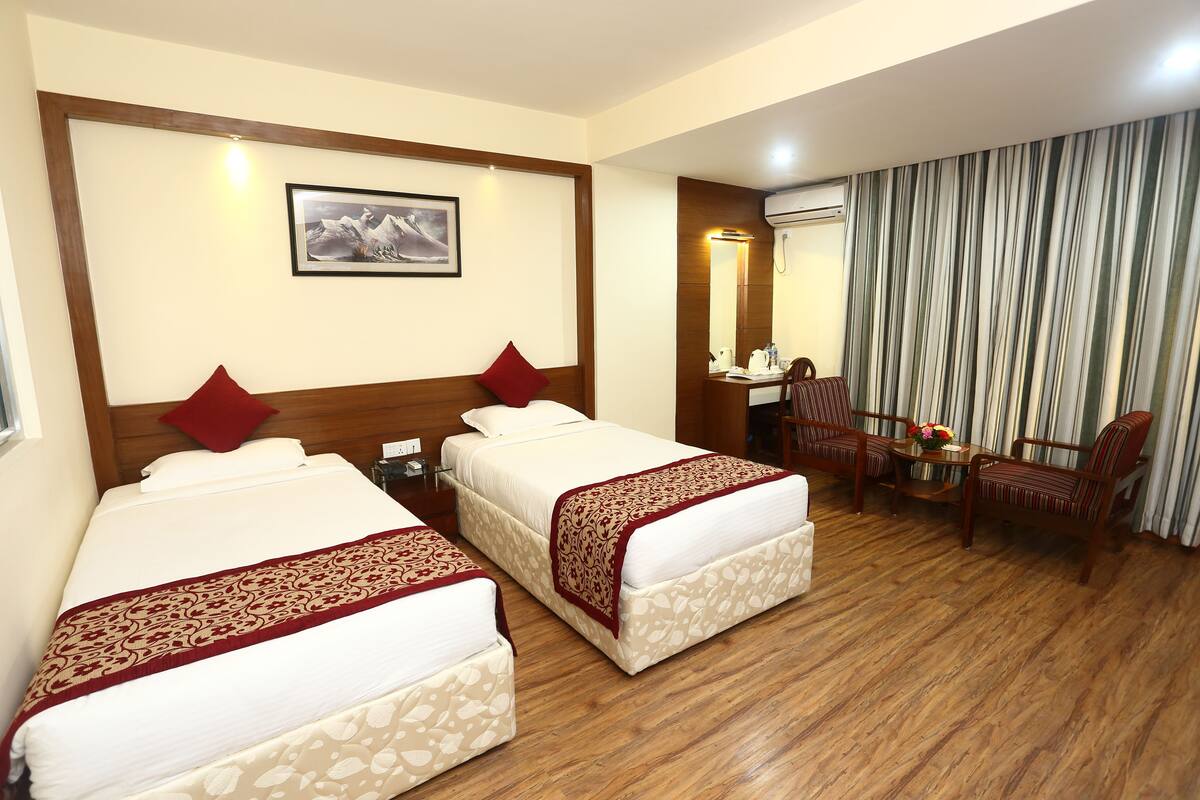 A hotel room with two beds, a desk with a chair, a mirror, and a window with curtains.