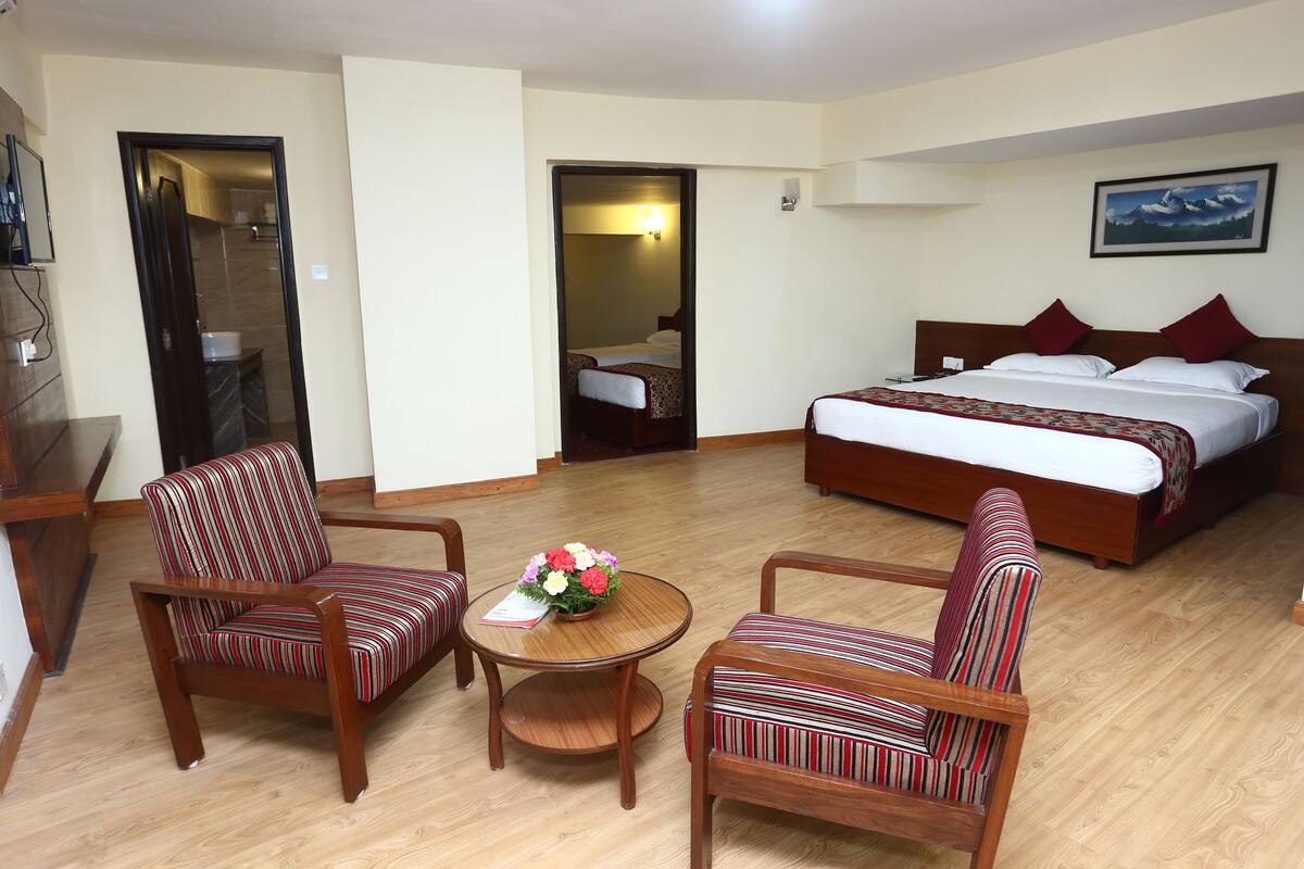 A hotel room with a large bed, two striped armchairs, a small wooden table with a vase of flowers, and a painting on the wall.
